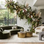 A contemporary luxury living room featuring a dramatic architectural moss and floral installation curving across the wall and ceiling, green velvet sofa, and gold coffee table.